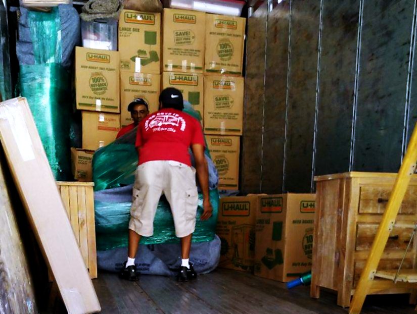 A crew member securing blanket-wrapped furniture against the wall of the truck