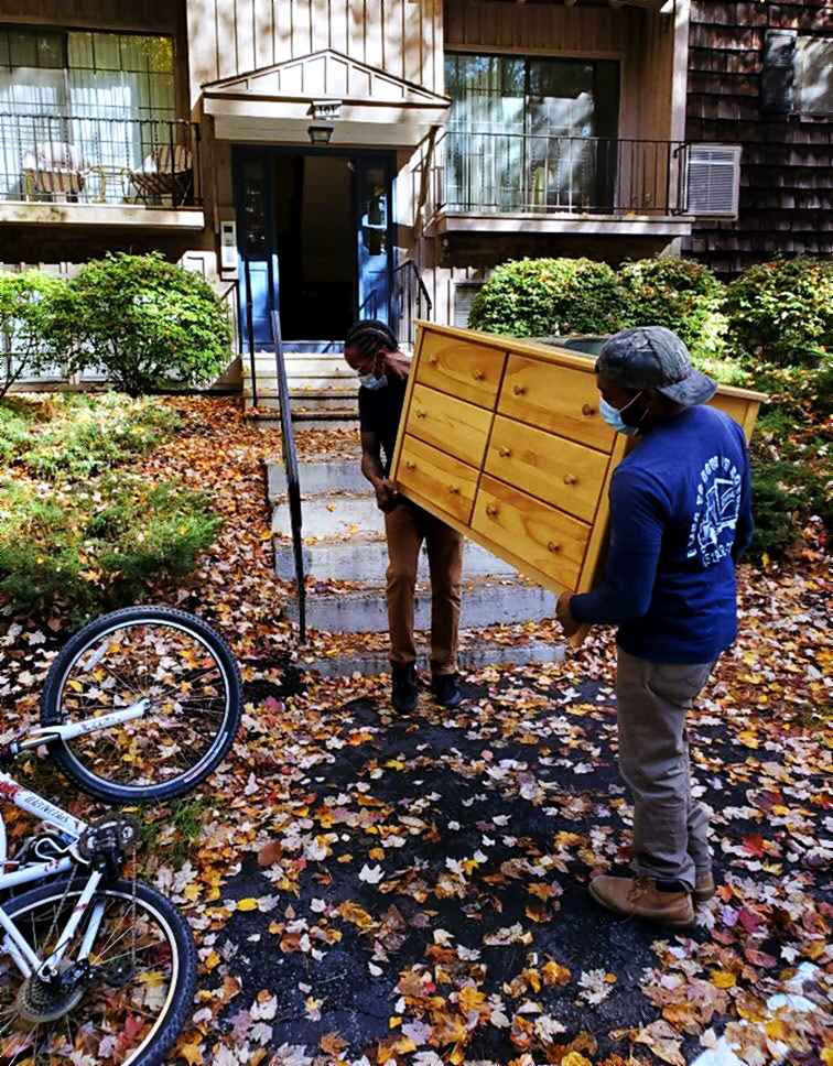 Two movers carrying a dresser up the front walk