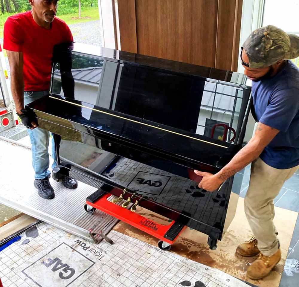Two movers rolling an upright piano on a piano dolly